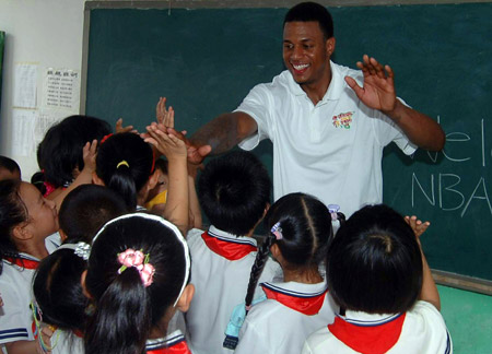 NBA player Brandom Rush claps with students of a primary school of rural migrant workers' children during the 2009 Basketball Without Borders Asia tour in Beijing, capital of China, July 30, 2009. NBA players donated computers to this school and helped build a basketball pitch before their visit. [Gong Lei/Xinhua]