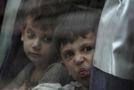 An internally displaced boy, who months earlier fled a military offensive against the Taliban in the Swat Valley region, makes a face towards a family member after boarding a bus to return to his home from a terminal in Karachi July 30, 2009. About 1,400 internally displaced persons (IDP), who were seeking shelter with their families in the southern seaport city of Karachi, departed on a 20-hour journey back to their villages, Reuters witnesses said. [Xinhua/Reuters]