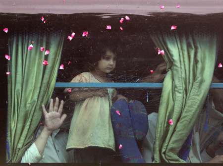 Rose petals, thrown by family members, fall past an internally displaced girl who boarded a bus to return to the Swat Valley region from Karachi July 30, 2009. About 1,400 internally displaced persons (IDP), who fled a military offensive against the Taliban in Swat months earlier, departed on a 20-hour journey back to their villages from the southern seaport Karachi, Reuters witnesses said. [Xinhua/Reuters]