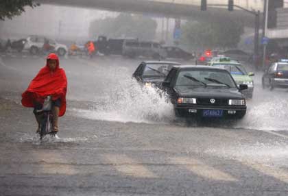 Surf's up ... a cyclist rides by cars on a flooded street in downtown Shanghai yesterday as most parts of the city suffered torrential rain that triggered an orange alert from the meteorological bureau. [Pei Xin/Shanghai Daily]