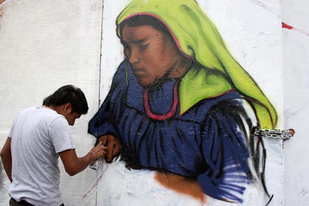 An graffiti artist paints on a 217-meter-long board near an art gallery in Mexico City, Aug. 2, 2009.[Xinhua]