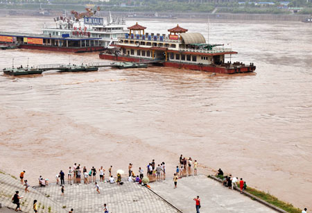 Local residents stand close to a wharf as the flood water of this year's highest level in the Yangtze River flows past southwest China's Chongqing Municipality, August 3, 2009. Emergency departments of the local authority are keeping high alert as some places were submerged.[Zhong Guilin/Xinhua]