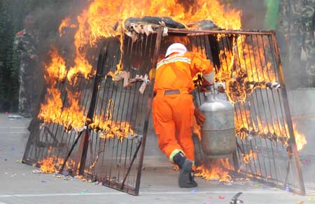 A Chinese fireman passes a fire gate carrying a LPG cylinder as he shows his skills for the public during a police camp open day in Jingdezhen city in east China's Jiangxi Province, August 4, 2009. [Shi Weiming/Xinhua] 