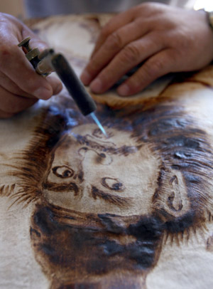 Folk artist Yu Hua paints with a 'fire brush' at home in Yongji City of north China's Shanxi Province, August 4, 2009. Yu Hua has created over 400 pieces of fire-painted artworks, since he created the special way of painting several years ago with a 'fire brush' scorching on the canvas made of white cloth and plank. [Xue Jun/Xinhua]