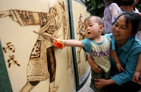 Neighbours of folk artist Yu Hua watch his creations at his house in Yongji City of north China's Shanxi Province, August 4, 2009. Yu Hua has created over 400 pieces of fire-painted artworks, since he created the special way of painting several years ago with a 'fire brush' scorching on the canvas made of white cloth and plank. [Xue Jun/Xinhua]