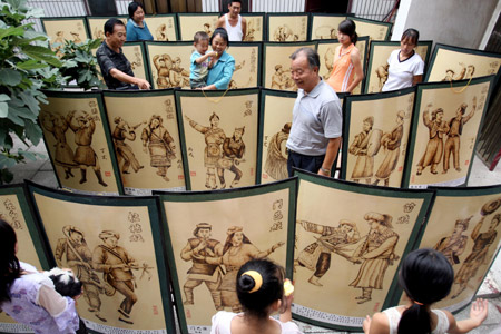 Neighbours of folk artist Yu Hua watch his creations at his house in Yongji City of north China's Shanxi Province, August 4, 2009. Yu Hua has created over 400 pieces of fire-painted artworks, since he created the special way of painting several years ago with a 'fire brush' scorching on the canvas made of white cloth and plank. [Xue Jun/Xinhua]