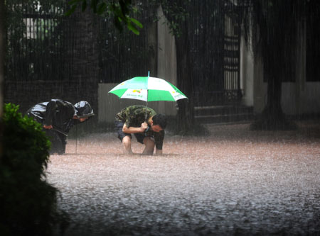 People stand on flooded street in China's Chongqing Municipality, Aug. 4, 2009. Heavy rain hit Chongqing on Tuesday causing traffic jam and the closure of highways. A total of 379,900 people are plagued by the strong rainfalls. [Yang Lei/Xinhua]