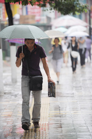 Pedestrians walk in the rain in a street in Guiyang, capital of southwest China's Guizhou Province, Aug. 4, 2009. [Liu Xu/Xinhua]