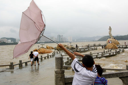 A Chinese tourist manages to hold his umbrella against strong wind on a trestle bridge on the beach near Zhuhai city in south China's Guangdong Province, August 4, 2009 as the tropical storm of 'Goni' approaches to the city. [Li Jianshu/Xinhua]