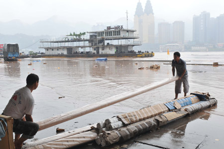 The workers of a logistics company move stock from the floodwaters in southwest China's Chongqing Municipality, August 4, 2009. The continual heavy rainfalls in Chongqing brought about flood over the city, with many lower sections of the riverside streets submerged. [Zhong Guilin/Xinhua]