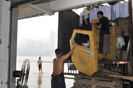 The workers of a logistics company move stock from the floodwaters in southwest China's Chongqing Municipality, August 4, 2009. The continual heavy rainfalls in Chongqing brought about flood over the city, with many lower sections of the riverside streets submerged. [Zhong Guilin/Xinhua]