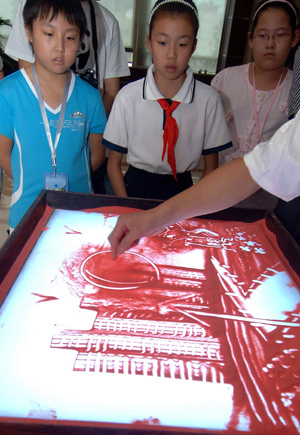 Students watch an artist painting a sand drawing with the theme of environmental protection during a launch ceremony of a project of energy conservation education in Beijing, capital of China, on Aug. 5, 2009. [Gong Lei/Xinhua]