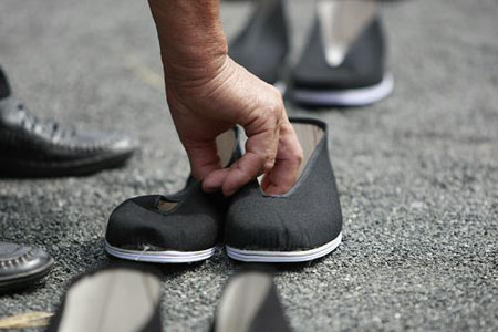 An man puts a pair of cloth shoes on the ground in memory of the dead Chinese forced laborer in a park in Tokyo, Aug. 9, 2009. [Ren Zhenglaig/Xinhua]