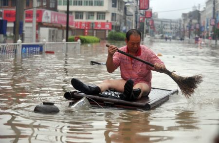 A man wade through the flooded street by home-made raft in Cangnan, east China's Zhejiang Province, Aug. 10, 2009. [Wang Dingchang/Xinhua]