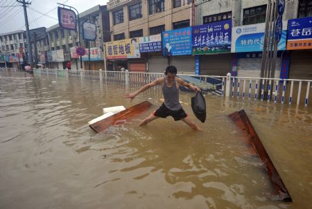 A man tries to stand after his raft fell apart in the flooded street in Cangnan, east China's Zhejiang Province, Aug. 10, 2009. [Wang Dingchang/Xinhua]