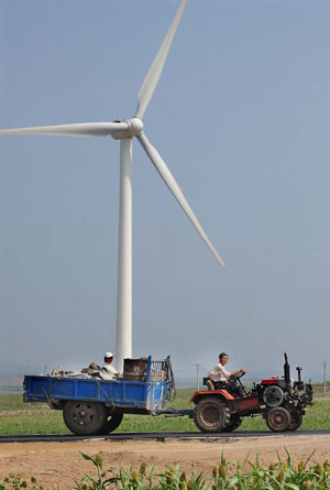 A tractor drives past a white turbine of wind power plants in Hinggan League (or prefecture) of north China's Inner Mongolia Autonomous Region on Aug. 7, 2009. Inner Mongolia, covering 1.18 million square kilometers of land, has boasted more than 3 million kilowatts of wind power, the largest of its kind in China. [Wang Song/Xinhua]
