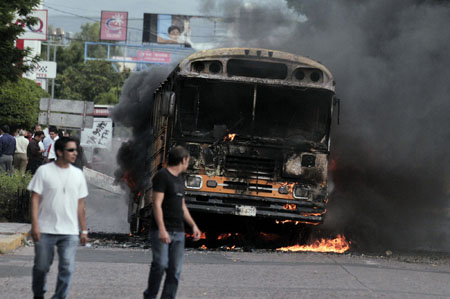 People walk by a burning bus after supporters of ousted Honduran President Manuel Zelaya set it on fire in Tegucigalpa, capital of Honduras, Aug. 11, 2009.