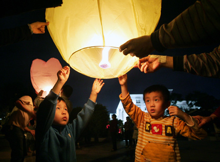 Kids under the help of their parents release the Kongming Lanterns into the air in Chuxiong Yi Autonomous Prefecture in southwest China's Yunnan Province, August 13, 2009.(Xinhua/Shi Sisi) 