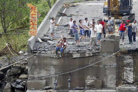 A man, sitting on a chair, moves past a destroyed bridge along cables slung by rescuers above a destroyed bridge in the village of Xinkai, Kaohsiung of Taiwan, August 12, 2009. The village was hit by debris flow caused by typhoon Morakot and casualties was estimated at at least 32. [CFP]
