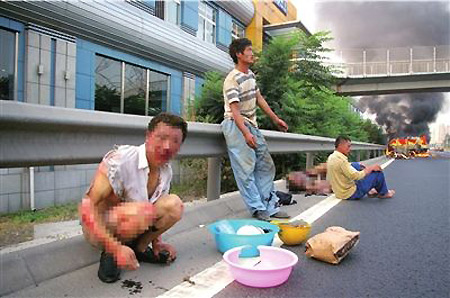 Slightly injured workers are seen sitting on the road with the burning minibus in the background in Beijing, August 13, 2009. [Xinhua