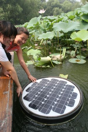 Visitors curiously touch a solar energy water cleaning device located in a lake in Zizhuyuan Park in Beijing, capital of China, Aug. 14, 2009. [Chen Xiaogen/Xinhua]