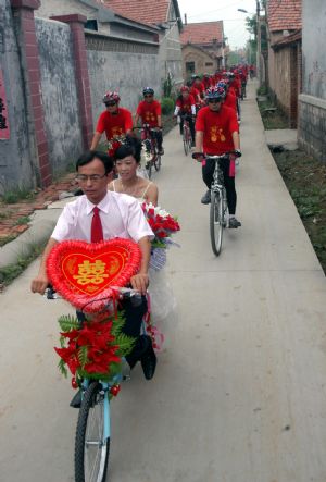 Bridegroom Tong Yanliang brings the bride home with a two-seat bicycle accompanied by their friends in Binzhou City of east China's Shandong Province, Aug. 19, 2009. Bridegroom Tong Yanliang and bride Li Jingjing held a special wedding by cycling accompanied by 99 bicycle fans called from the internet. [Li Rongxin/Xinhua]
