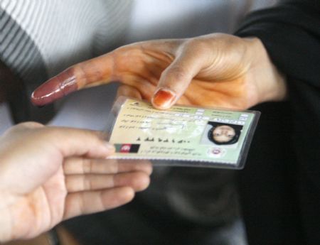 A woman shows an ink-stained finger as she hands over her identification card in order to vote in the presidential elections at a polling station in Kabul, August 20, 2009. Streets in Afghanistan were mainly quiet and tense early on Thursday as Afghans headed to the polls for an anxiously awaited presidential election that Taliban fighters have vowed to disrupt.[Xinhua/Reuters]