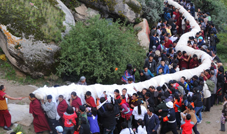 Lamas and locals carry a huge-sized Buddha Thangka painting to the site where the Buddha Thangka painting unfolding ceremony is held in Zhebung Monastery on the outskirts of Lhasa, capital of southwest China's Tibet Autonomous Region, on Aug. 20, 2009.[Chogo/Xinhua]