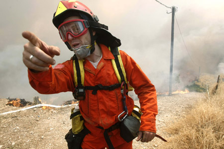 A fireman gestures as a forest fire burns in Varnava village, northeast of Athens, August 22, 2009.