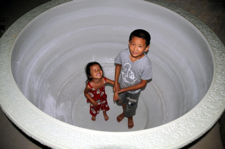 Two kids stand inside a colossal crock of black and white porcelain, which stands at 1.36 meters in height, measures 6.8 meters in perimeter, with a caliber of 2 meters and a weight of over 1,500 kg, in Jingdezhen, east China's Jiangxi Province, Aug. 24, 2009.[Shi Weiming/Xinhua]