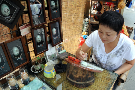 Tao Rong, a crafts artist from Sichuan Province, draws on an egg shell in the ancient Jinli street in Chengdu, capital of southwest China&apos;s Sichuan Province, Aug. 24, 2009. The ancient Jinli street is a popular tourist spot known for its unique ancient architecture styles and the local handicrafts in Chengdu.(Xinhua Photo)