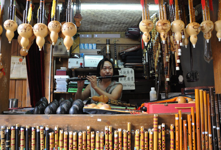 Folk artist Su Fangyuan plays flute in the ancient Jinli street in Chengdu, capital of southwest China's Sichuan Province, Aug. 24, 2009.(Xinhua Photo)