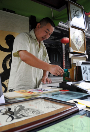 Folk artist Luo Baichuan draws a painting in the ancient Jinli street in Chengdu, capital of southwest China's Sichuan Province, Aug. 24, 2009. (Xinhua Photo)