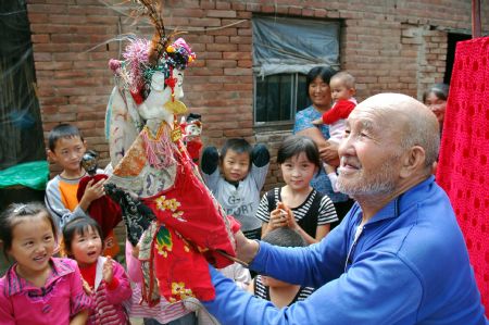 Yuan Youen, a folk artist, performs Shoulder Pole Drama, a local traveling puppet drama show the performer of which loads the stage property by a shoulder pole, in Balizhuang Village in Neihuang County, central China's Henan Province, Aug. 23, 2009.
