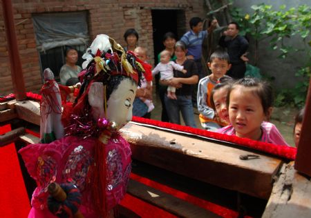 Children watch Yuan Youen, a folk artist, perform Shoulder Pole Drama, a local traveling puppet drama show the performer of which loads the stage property by a shoulder pole, in Balizhuang Village in Neihuang County, central China&apos;s Henan Province, Aug. 23, 2009. 