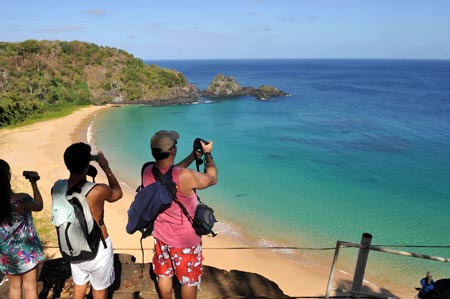 Tourists take photos at the Concessao beach in Fernando de Noronha Island, northeastern Brazil, Aug. 25, 2009. Fernando de Noronha, well-preserved with its beautiful view, pure seawater and various marine lives, was listed as a world natural heritage site by the UNESCO in 2001. [Song Weiwei/Xinhua]