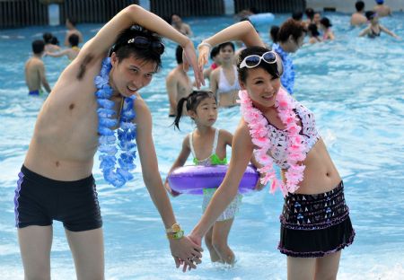 A newly-wedded couple poses for photos during a group wedding ceremony held in the swimming pool at Happy Valley, a famous theme park in Shenzhen, south China's Guangdong Province, August 26, 2009. Thirty newly-wedded couples took part in the group wedding ceremony held in the swimming pool here on Wednesday. [Yuan Shuiling/Xinhua]