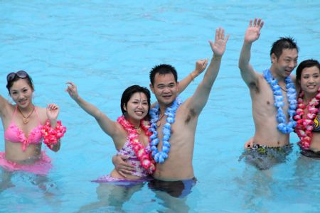 The newly-wedded couples greet people in the water during a group wedding ceremony held in the swimming pool at Happy Valley, a famous theme park in Shenzhen, south China's Guangdong Province, August 26, 2009. Thirty newly-wedded couples took part in the group wedding ceremony held in the swimming pool here on Wednesday. [Feng Ming/Xinhua] 