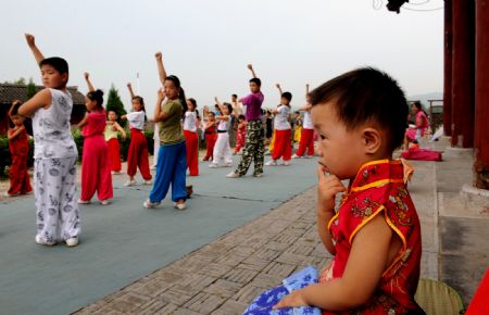A boy watching children who practise martial arts sits on the remedied ancient city-wall in Shouxian County, a famous historic and cultural site in east China's Anhui Province, on Aug. 17, 2009.(Xinhua/Tao Ming) 