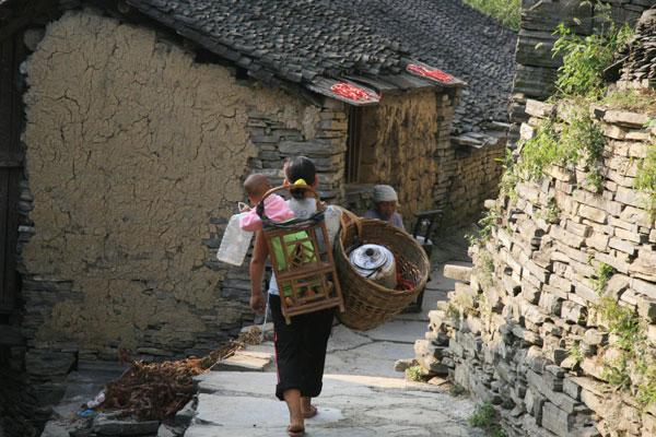 A woman with her small child in the wooden basket on her back, walks down the cobble stone path in Miao People's Village. [Photo:CRIENGLISH.com/Duan Xuelian]