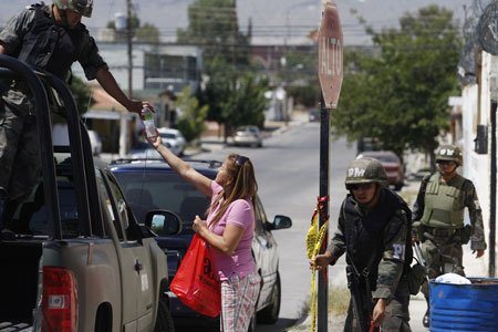 A resident gives a bottle of water to a soldier guarding a crime scene in the border city of Ciudad Juarez, September 6, 2009. Two members of a gang were killed inside a house where police also found a stash of marijuana, submachine guns and pistols, according to local media.[Xinhua/Reuters]