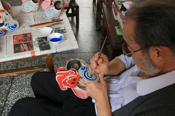 Nie Fangjun adds colors to the pasted-paper sculpture of a lion head. [Photo: CRIENGLISH.com/Duan Xuelian]