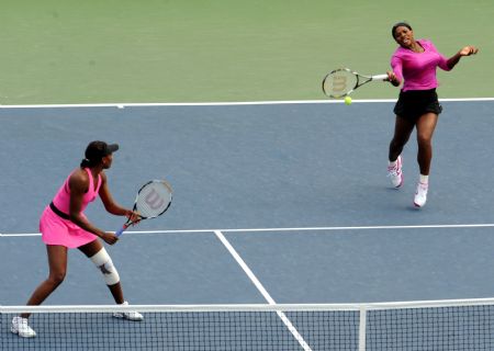 Serena Williams (R) of the US returns a shot as her sister Venus Williams watches during the women's doubles quarter final against Zheng Jie and Yan Zi of China at the U.S. Open tennis tournament in New York, the U.S., Sept. 9, 2009.(Xinhua/Shen Hong)