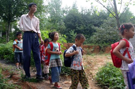 Shao Jun (L) escorts his pupils on their way home in Sanbing Township of Chaohu City, east China's Anhui Province, Sept. 8, 2009. Shao, 42 years old, lost his right arm during an accident at the age of 19. He started teaching at Dongshan Primary School in 1998 and spent 11 years there. As high-grade pupils were gradually transferred to downtown schools, there is one class in the school with only eight pupils. (Xinhua)