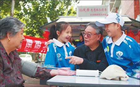 Volunteer Sun Maofang (2nd, R), 66, show young volunteers how to use a blood pressure monitor in Beijing yesterday. [China Daily