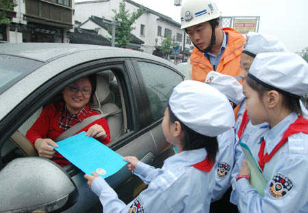 A young volunteer hands out promotion leaflet of 'going out green' to a car driver on a street in Suzhou, east China's Jiangsu Province, Sept. 22, 2009. This Tuesday is China's third Car-Free Day and people are encouraged to walk, ride bikes or take buses instead of driving their cars. [Zhu Guigen/Xinhua]