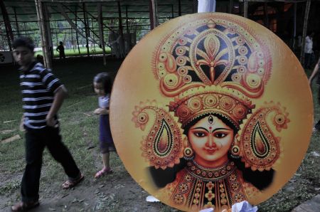 People pass by a board imprinted with an image of Hindu Goddess Durga at a makeshift temple one day ahead of Durga Puja, the biggest religious festival of Hindus, in Dhaka, capital of Bangladesh, on Sept. 23, 2009. The five-day festival will start from Thursday. (Xinhua/Qamruzzaman)