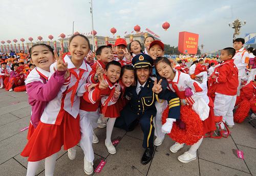 Primary school children participating the ceremony pose for photos with a solider from the PLA Military Music Orchestra