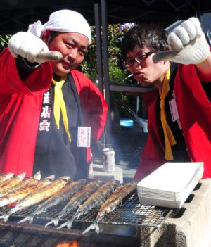 Two men pose with their grill saury fish on a street during a saury event in Tokyo, capital of Japan, Oct. 11, 2009. Some 2,000 saury fish, a popular seafood used in Japanese cuisine, will be distributed to people during the autumn event.[Hua Yi/Xinhua]