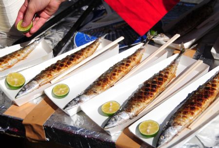 A men displays grill saury fish on a street during a saury event in Tokyo, capital of Japan, Oct. 11, 2009.[Hua Yi/Xinhua]